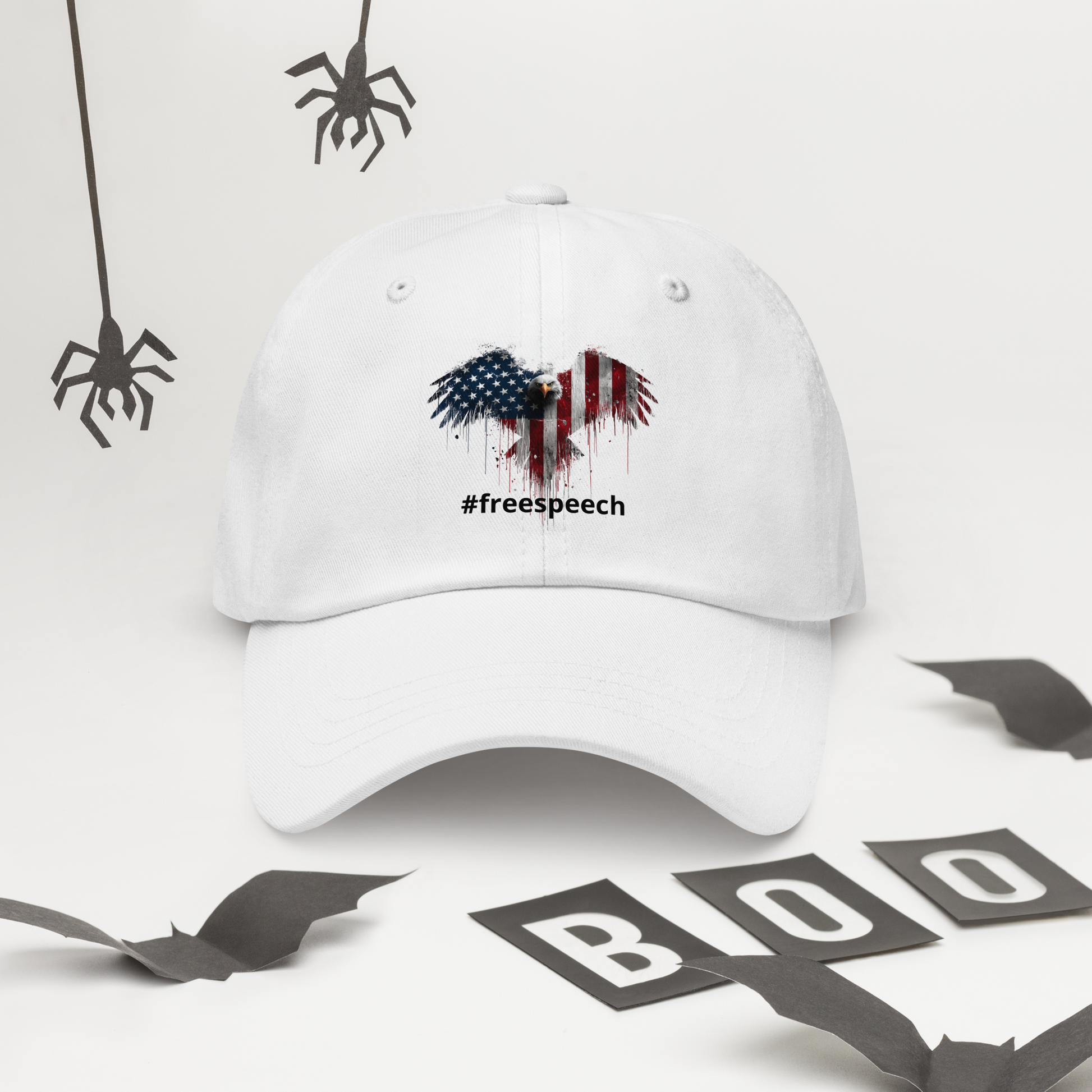 White cap with '#freespeech' design on a white background with black ribbons and spiders.
